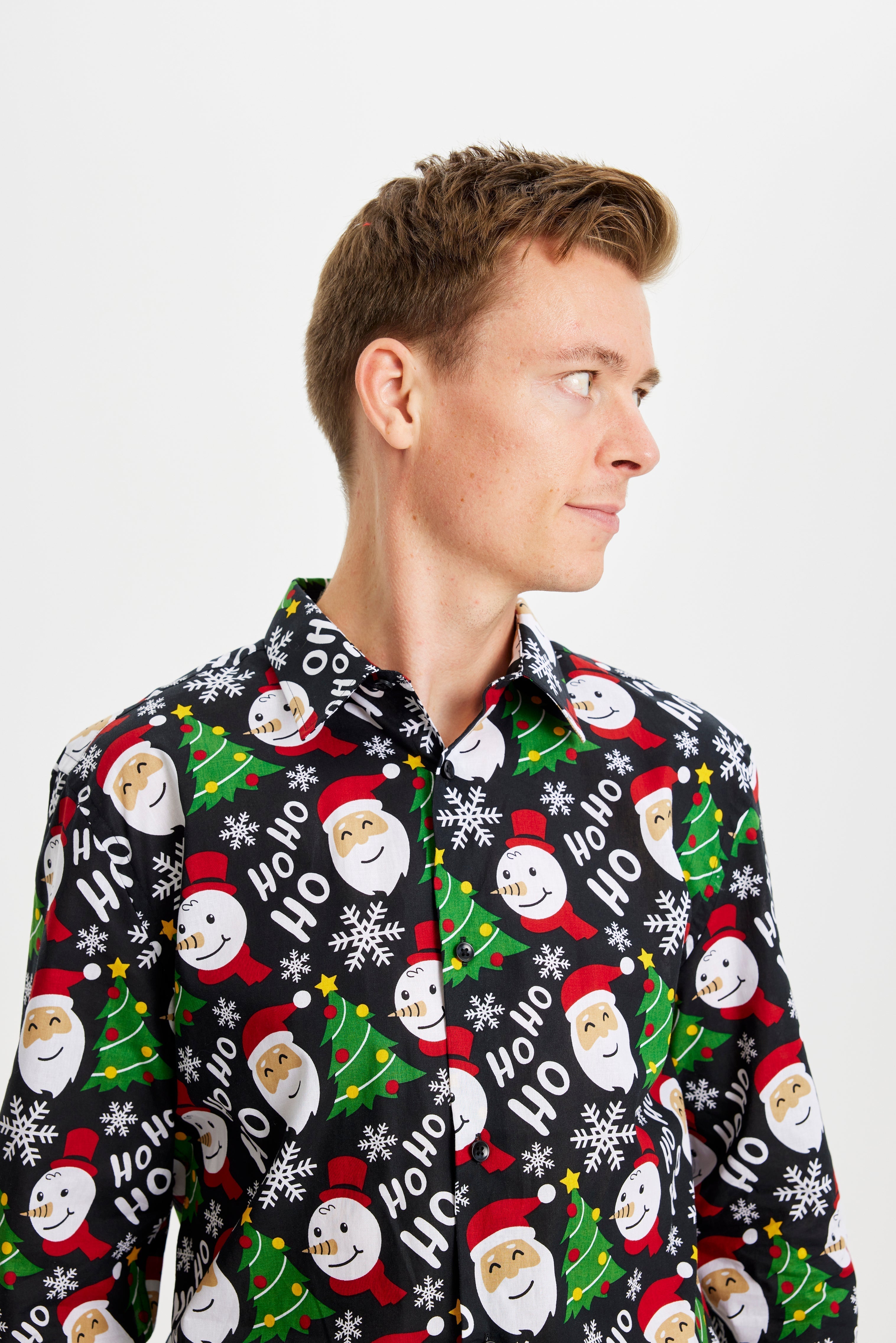 Un homme qui pose regarde sur le côté et porte une chemise de Noël noire à motifs.